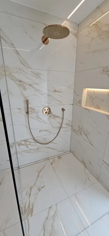 Indbygget bruseløsning med messingfarvede armaturer og en belyst niche.