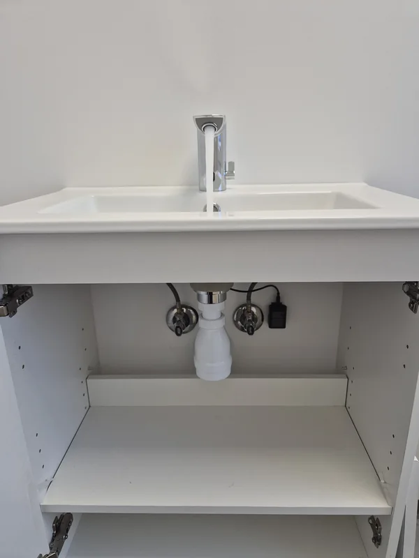 Monteret håndvask med synlige tilslutninger, ventiler og vandlås.